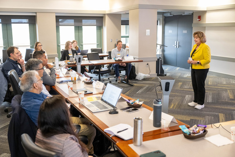 UI President Barbara Wilson, dressed in a gold blazer, addresses the AI Industry Advisory Board members in a conference room.